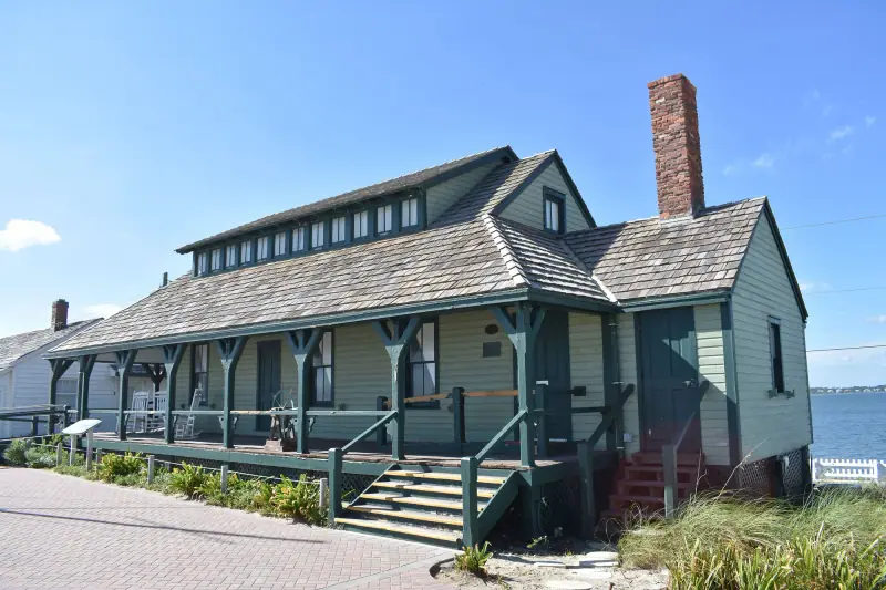 Two-story wooden House of Refuge with green trim and a wide porch under a blue sky